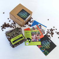 Overhead view of Swelter Coffee's gift box with sample bags of three different coffees inside, and the farmer's card inserts, next to a vase of flowers on a wood table