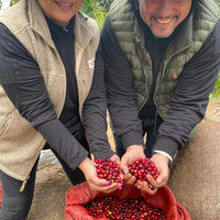 Lilly and David showing red coffee cherries freshly picked, smiling at the camera