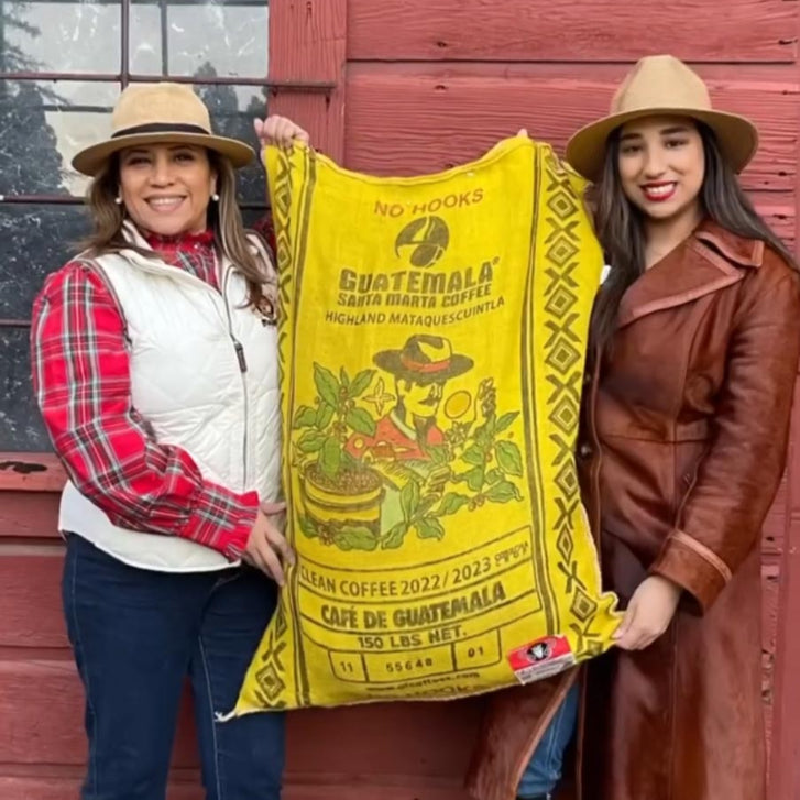 Lilly and Sabrina holding up a bag of green coffee with their branding