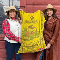 Lilly and Sabrina holding up a bag of green coffee with their branding