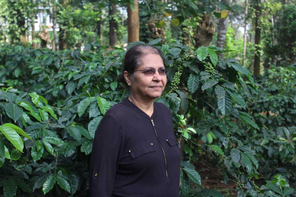 Portrait of Poornima in front of coffee trees on her farm in southern India