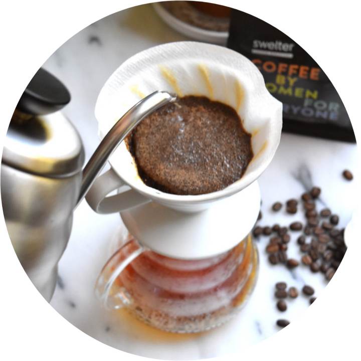 View of a kettle pouring hot water into a V60 brewer, with beans scattered on the table and a bag in the background