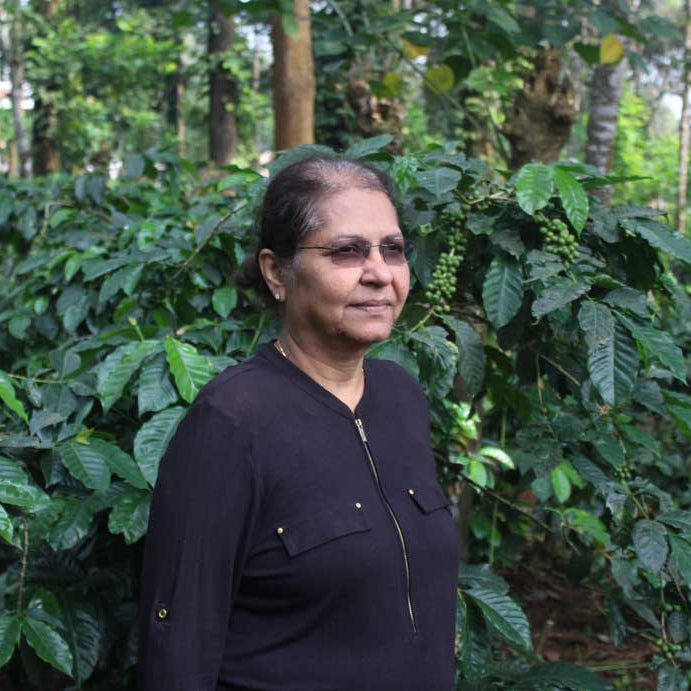 Portrait of Poornima in front of coffee trees on her farm in southern India