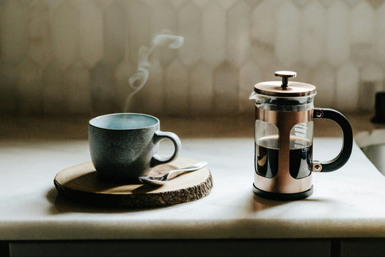 A french press brewing coffee on a table next to a coffee mug