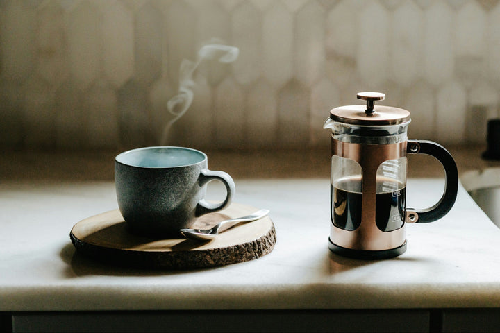 A french press brewing coffee on a table next to a coffee mug