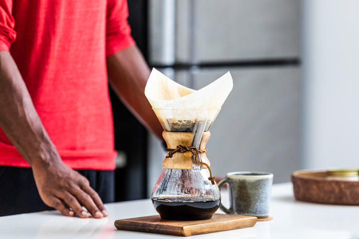 A man standing next to a Chemex coffee brewer as it brews a fresh cup of coffee